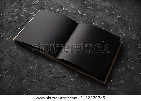 Photo. Open blank black brochure on black plaster background. Mock-up for graphic designers portfolios.