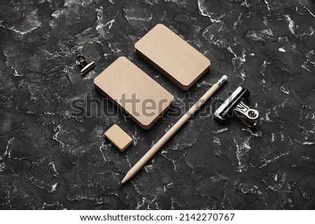 Blank kraft business cards, pencil, eraser and clip on black plaster background. Blank stationery set.