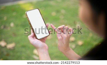 Female hands holding a smartphone white screen mockup against blurred green park background. closeup