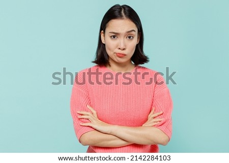 Young sad offended shrewd woman of Asian ethnicity 20s wearing pink sweater hold hands crossed folded isolated on pastel plain light blue color background studio portrait. People lifestyle concept. Royalty-Free Stock Photo #2142284103