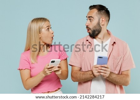 Young shocked happy couple two friends family man woman in casual clothes hold in hand use mobile cell phone look to each other together isolated on pastel plain light blue background studio portrait