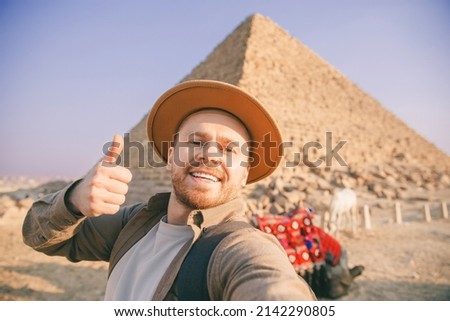 Selfie photo archaeologist man in hat with camel background pyramid of Egyptian Giza, sunset Cairo, Egypt.