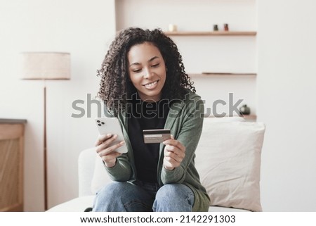 Young smiling woman holding credit card, using smartphone. Paying online, home shopping, e-commerce, internet banking, spending money, finance, electronic store concept Royalty-Free Stock Photo #2142291303