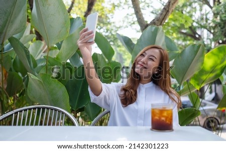Portrait image of a beautiful young asian woman using mobile phone to take a selfie in cafe