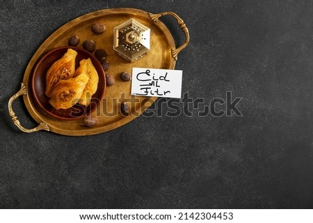 Tray with tasty Turkish baklava, fanoos lamp and greeting card for for Eid al-Fitr (Feast of Breaking the Fast) on dark background Royalty-Free Stock Photo #2142304453