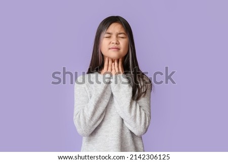 Ill Asian girl with sore throat on color background
