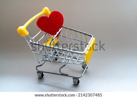 Shopping basket on a gray background with a bright red heart. Close-up.