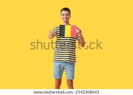 Young man with flag of Belgium showing thumb-up on color background