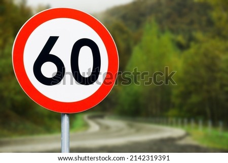 Speed limit sign with curvy road behind. Maximum sixty kilometers per hour. Safety on road background. White round sign red border line. Traffic ticket background. Speeding fine. Slow down on turn.