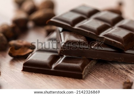 Chocolate bar with a wooden background surrounded by roasted cocoa beans