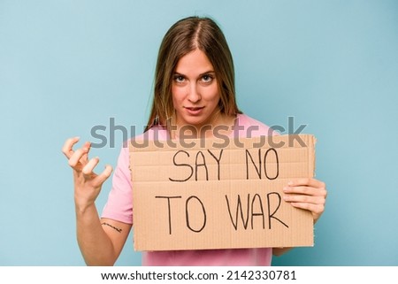 Young caucasian woman holding no war placard isolated on blue background