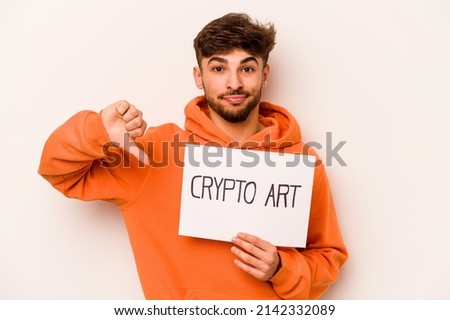 Young hispanic man holding a crypto art placard isolated on white background showing a dislike gesture, thumbs down. Disagreement concept.
