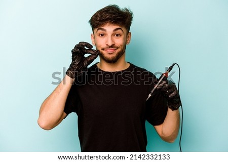 Tattoo artist hispanic man isolated on blue background with fingers on lips keeping a secret.