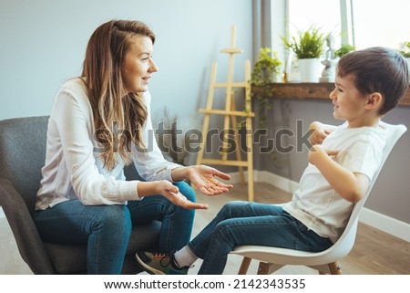 Cheerful young kid talking with helpful child counselor during psychotherapy session in children mental health center. Child counselor during psychotherapy session Royalty-Free Stock Photo #2142343535
