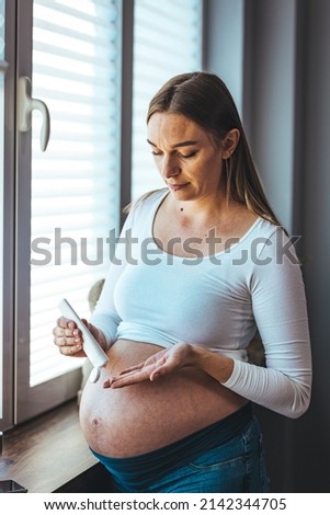 Close up of pregnant women applying moisturizer. Cheerful mother applying cream on her belly. Pregnant women putting anti stretch creme on her belly.