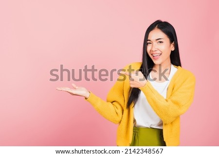 Portrait Asian beautiful young woman smiling standing pointing finger out on pink background, Thai happy face excited female point into empty looking to side away with copy space for text Royalty-Free Stock Photo #2142348567