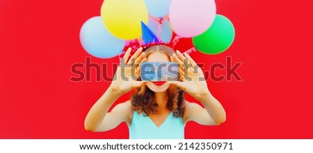 Happy woman in birthday hat taking selfie by smartphone with stretching her hands on colorful balloons on red background