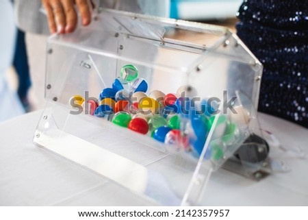 Process of prize drawings, extracting a winning numbers of lottery machine, raffle drum with a bingo balls and winning tickets on event with a host and hands on lottery machine
