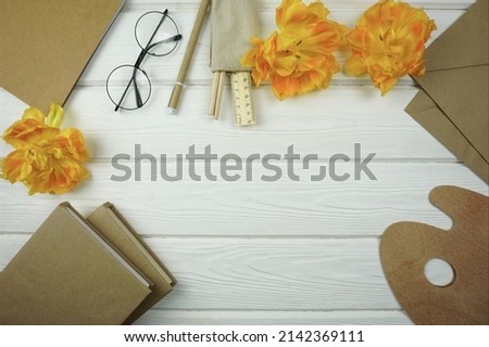 Yellow tulips and office supplies of natural color lie on a light wooden background                    
