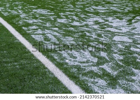 The football field with artificial green grass is covered with a light layer of snow. Early spring. Green grass on the football field is visible from under the snow. Amateur football field.