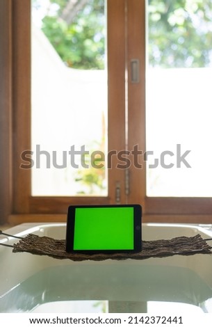 Tablet on a stand in the bathroom against the background of the window. Chroma key screen, mockup. 