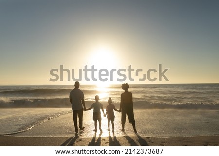 Full length rear view of african american family holding hands while looking at sunset over sea. unaltered, family, lifestyle, togetherness, enjoyment and holiday concept. Royalty-Free Stock Photo #2142373687