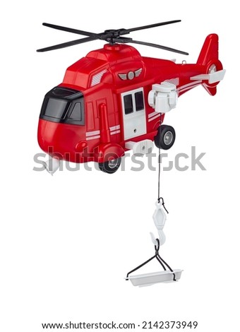 Red toy rescue helicopter with a rescue cradle on a cord, isolated on a white background. Rescue and evacuation from hard-to-reach places. High quality photo. Royalty-Free Stock Photo #2142373949