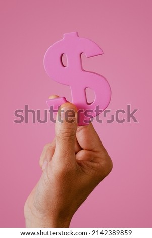closeup of a young man grabbing a pink dollar sign on a pink background, depicting the pink money or pink capitalism concepts