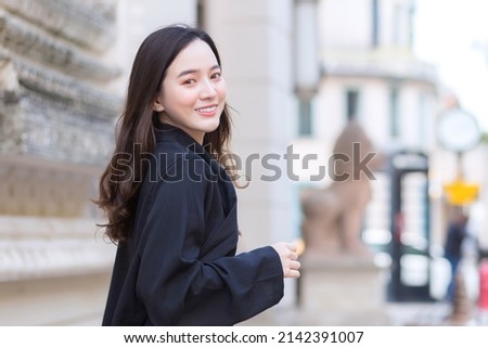 A picture of a beautiful long haired Asian beautiful woman in a black robe smiling happily walking and looking out in the city outdoors.
