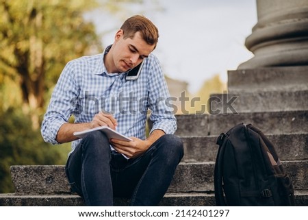 Handsome student sitting on stairs of university and studying
