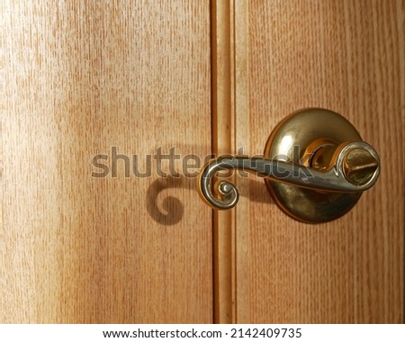 Brass doorknob with lock on wood door. Ash texture, fillet. Interesting double shadow with a spiral from the door handle. Element of interior in warm colors. Sun flare. Focus on foreground. Copy space Royalty-Free Stock Photo #2142409735