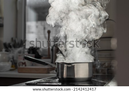 Boiling water with steam in a pot on an electric stove in the kitchen. Blurred background, selective focus. Royalty-Free Stock Photo #2142412417