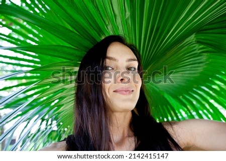 Young beautiful Woman with dark hair takes a selfie on the background of green tropical leaf. Traveler Woman on the background of palm tree. Solo Female Traveler. Summer concept. Bangkok, Thailand.