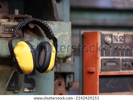 Yellow protective ear muffs hang on machines in heavy industrial plants. The concept is a PPE device that protects against loud noise in the operator's environment. industrial work safety equipment Royalty-Free Stock Photo #2142429251