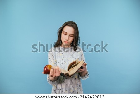 Attractive lady in a dress reads a book with a serious face and holds an apple in his hand