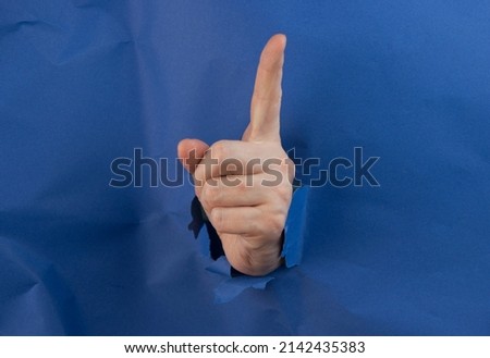 Female fist punching through blue paper background. War, struggle, conflict, feminist concept. Banner with copy space.
