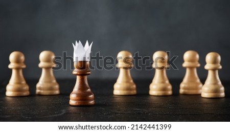 Ambitious pawn with paper crown aspires to be a king and confronts the rivals. Business entrepreneurship, aspiration, confrontation and leadership concept. Royalty-Free Stock Photo #2142441399