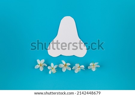 Paper silhouette of a nose and spring flowers on a blue background. Seasonal allergy concept. Flat lay, place for text.