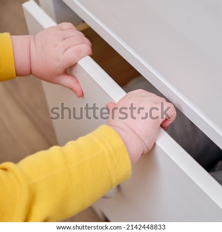 Danger for the baby to pinch the hand of the cabinet door or chest of drawers. Protect children from home furniture, kids safety Royalty-Free Stock Photo #2142448833