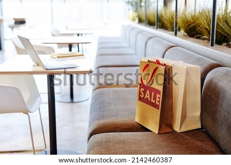 Background image of paper shopping bags with red SALE sign on seat in empty food court at shopping mall, copy space