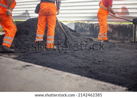 A bunch of asphalt. Workers repair the road. People in orange clothes. Asphalt pavement. Men work with shovels. Royalty-Free Stock Photo #2142462385