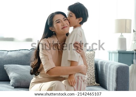 Happy Asian tender son kisses mother on mother's day during holiday celebration at home.