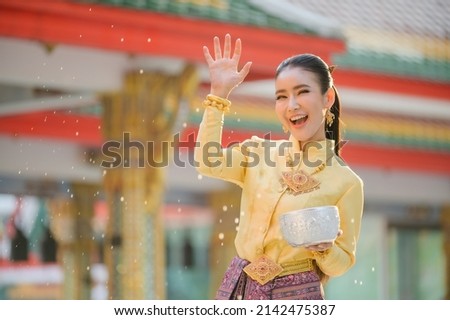 Beautiful Thai girls in Thai costumes hold water bowls and sprinkle water with their hands on Songkran Festival or Thai New Year's Day Royalty-Free Stock Photo #2142475387