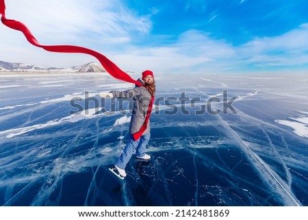 Happy woman tourist on ice skates and with long red scarf on frozen lake Baikal. Concept winter tourism freedom.