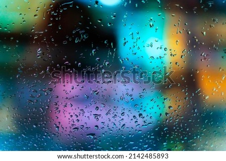 Rain on the window and bokeh city lights. Rainy night in the urban street at night. View through glass window, blurred motion. Seasons, weather concept. Selective focus on droplet