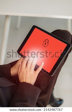 Close-up of female hand in office using laptop and tablet with creative red web security screen or closed access. The concept of secure information.