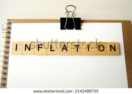 On the table is a notebook, a sheet of paper, an inscription made of wooden cubes with the word inflation.  The concept of minimalism, raising prices.  Close-up, copy space for text.