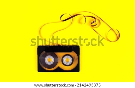 Audio cassette with pulled out audiotape on yellow background
