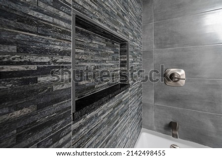 Renovated modern bathroom with bathtub. Dark (Black Grey) tiles accent wall and niche with Grey tiles and white bathtub.  Royalty-Free Stock Photo #2142498455