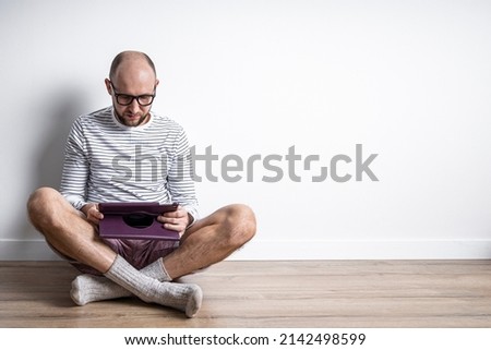 Young man in glasses with a tablet sitting on the floor 
